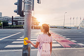 The girl presses the button on the traffic light to turn green and cross the road safely