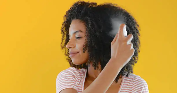 Cropped shot of a young woman spraying her hair with hairspray