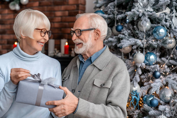 senior mann gibt ein weihnachtsgeschenk an seine frau zu hause - gift new year couple men stock-fotos und bilder
