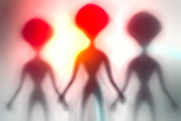 istock Silhouettes of spooky aliens and bright light on behind them 1187807600