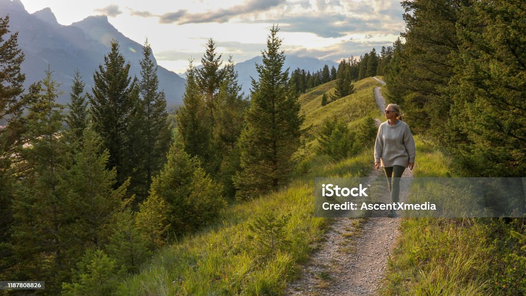 Mature woman walks down trail in the morning She looks out to mountain ranges in distance Walking Stock Photo