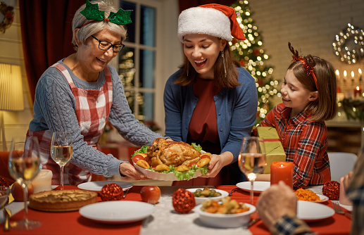 Merry Christmas and Happy New Year! A beautiful living room decorated for holidays. Table served to the dinner. Women are holding turkey.