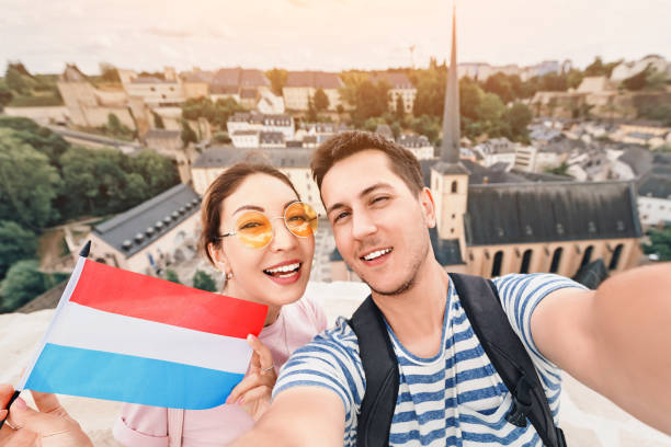A happy couple of young people hug and take selfies with the flag of Luxembourg while sightseeing in old town. Tourism, immigration and education for students in Europe concept A happy couple of young people hug and take selfies with the flag of Luxembourg while sightseeing in old town. Tourism, immigration and education for students in Europe concept luxemburg stock pictures, royalty-free photos & images