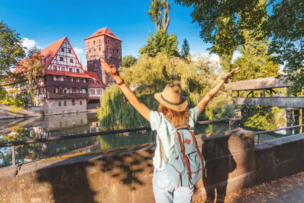 Photo of Happy asian woman tourist enjoying sunset view of the old town of Nurnberg city and Pegnitz river. Travel and student lifestyle in Germany