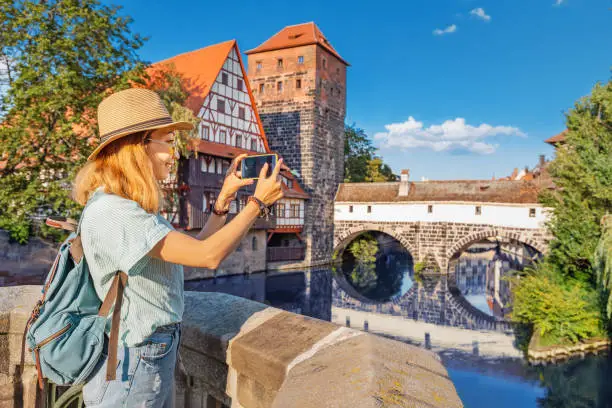 Happy asian woman tourist taking photo of the old town of Nurnberg city and Pegnitz river. Travel blogger in Germany concept