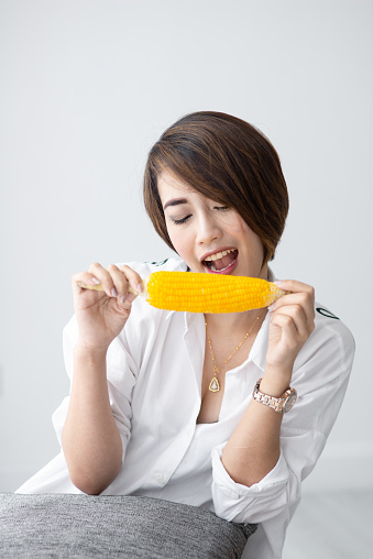 Asian girl eating yellow corn at home.