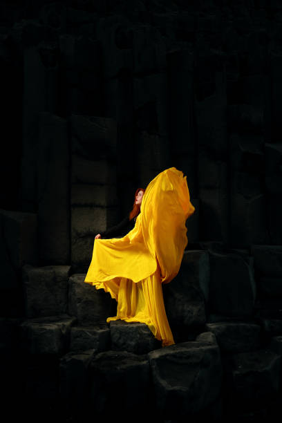 Fashion model wearing yellow skirt posing on black basalt rocks in Iceland, looking away