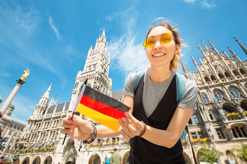 A happy girl with a German flag poses against the background of the city hall in Munich. Travel and immigration to Germany