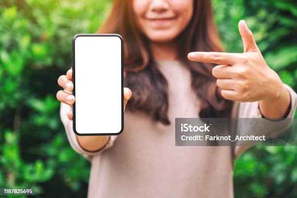 A Woman Holding And Pointing Finger At A Black Mobile Phone With Blank Desktop Screen In The Outdoors - Fotografias de stock e mais imagens de Apontar - Sinal Manual