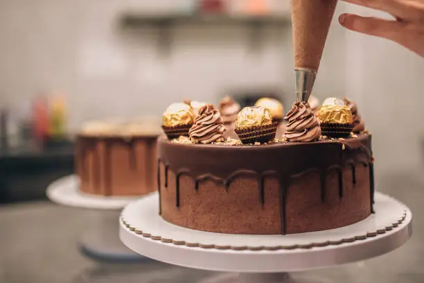 Photo of Confectioner decorating chocolate cake, close-up.