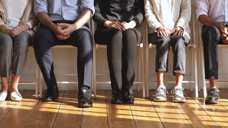 Professional unemployed business people sit on chairs, legs closeup view