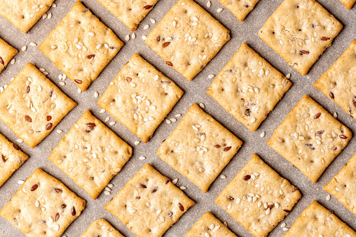 Homemade freshly baked crackers with flax and sesame seeds are laid out on baking paper, top view. Cracker background.