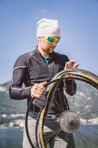 Bike Repair. Man Repairing Mountain Bike. Cyclist man in trouble rear wheel wheel case of accident. Man Fixes Bike near lake in Italy background mountains. cyclist repairing bicycle wheel outdoors. reparación de bicicletas. hombre reparando bicicleta de montaña. hombre ciclista en problemas de la rueda trasera caso de accidente. man fixes bike cerca del lago en italia montañas de fondo. ciclista reparando la rueda de la bicicleta al aire libre