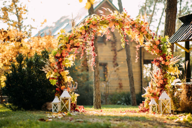 Wedding arch is on the background of autumn trees and house. Wedding arch of autumn leaves, flowers and cereal ears is on the background of autumn trees and house. country wedding arches stock pictures, royalty-free photos & images