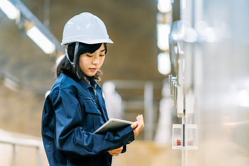 A young female engineer is working at engineering facility and checking a digital tablet.