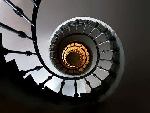 ancient spiral staircase seen from below with the decorated wrought-iron handrail and the skylight above. Night shot inside an ancient building