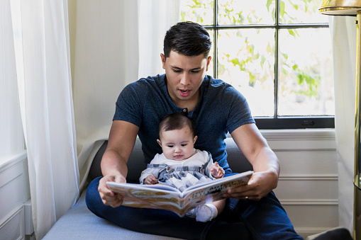 Sitting by window, dad reads book to baby