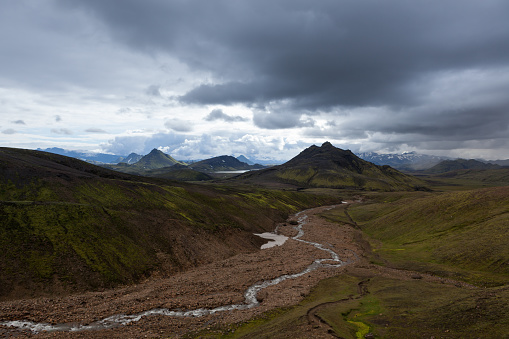 Dramatic Iceland landscape with green mountains covered with thick Icelandic moss and river on a gray moody cloudy day.