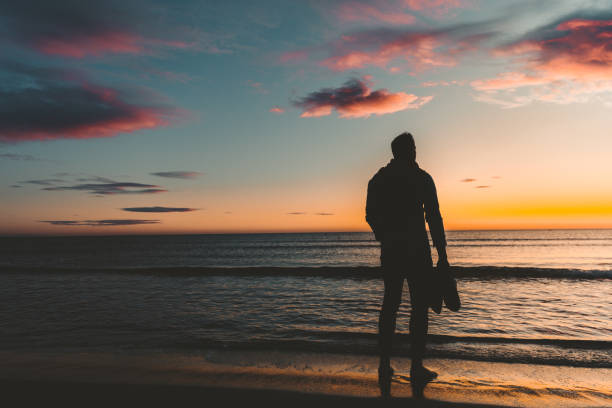 istock Young man walking down the beach at sunrise. 1187858527