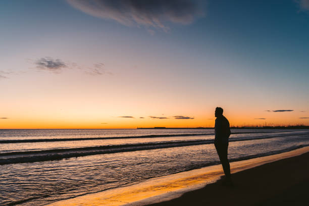 istock Young man walking down the beach at sunrise. 1187859231