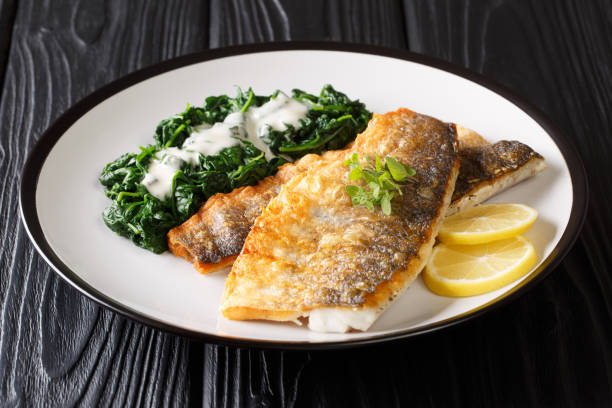 健康的なバーベキューシーバスフィレとほうれん草のクローズアップをプレートに盛り付けます。水平 - prepared fish fish grilled close up ストックフォトと画像