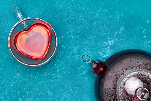 top view of red hibiscus tea in glass teapot and heart shaped cup on blue table