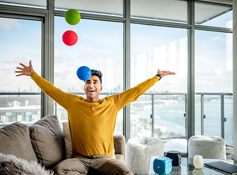 Young Indian man playing with colorful balls in her living room. View of the modern city in the background.