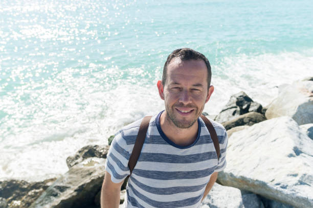 istock Young smiling man standing on sea rocks looking to camera 1187876271