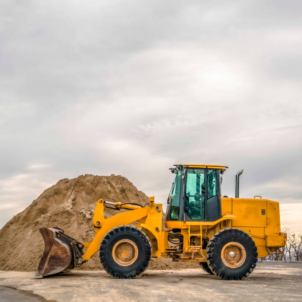 istock Square frame Bulldozer in front of a mound of soil with leafless trees and cloudy sky background 1187876656
