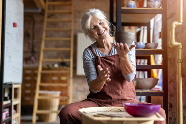 Elderly woman making ceramic work with potter's wheel Hand made ceramics are formed by a mature woman on a potters wheel hobbies stock pictures, royalty-free photos & images