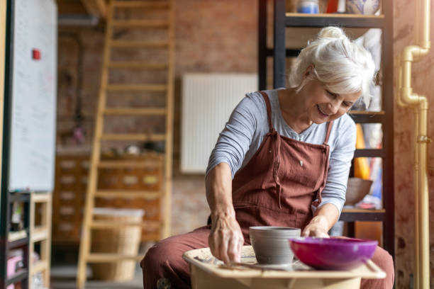 Elderly woman making ceramic work with potter's wheel Hand made ceramics are formed by a mature woman on a potters wheel pottery making stock pictures, royalty-free photos & images