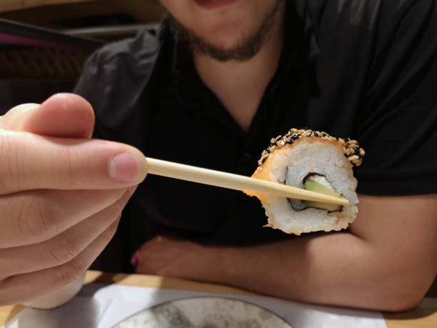 istock Latin young man with a salmon california roll maki picked with chopsticks 1187882425