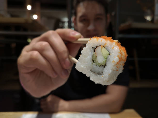 istock Latin young man with a california roll maki picked with chopsticks 1187883612