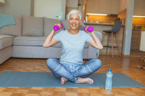 mujer mayor haciendo ejercicios de fitness frente a la televisión. - exercices fotografías e imágenes de stock