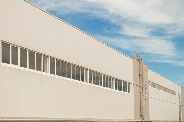istock Facade of a long multi-span industrial building under a blue cloudy sky. Gray wall with staircase and tape glazing windows. 1187889332