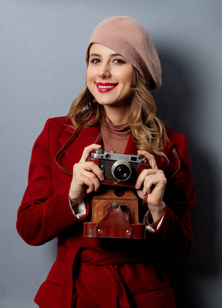 Young woman in red coat with camera on grey background