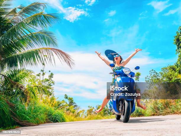 Crazy Funny Woman Catching Flying Hat Riding A Motorbike On A Blue Sky And  Green Tropics