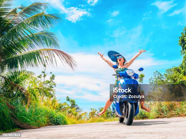 Crazy Funny Woman Catching Flying Hat Riding A Motorbike On A Blue Sky And Green Tropics Crazy Funny Woman Catching Flying Hat Riding A Motorbike On A Blue Sky And Green Tropics
