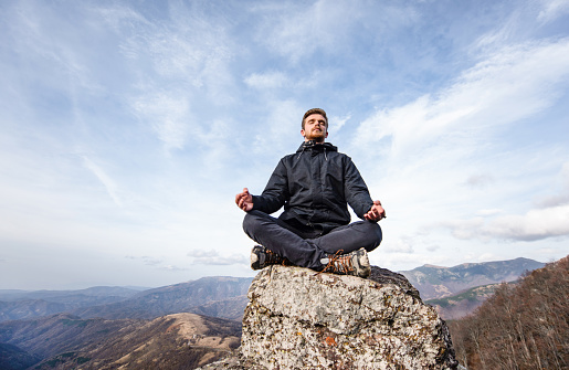 Young man meditating on mountain top.