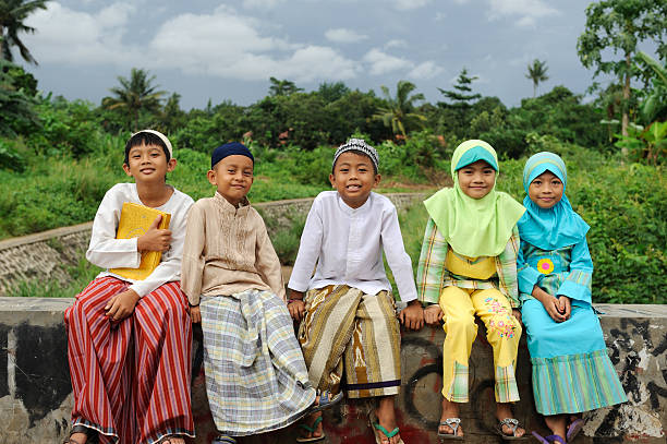 Five smiling young Muslim kids sitting on a brick wall Group of Muslim kids, sitting on bridge indonesian ethnicity stock pictures, royalty-free photos & images