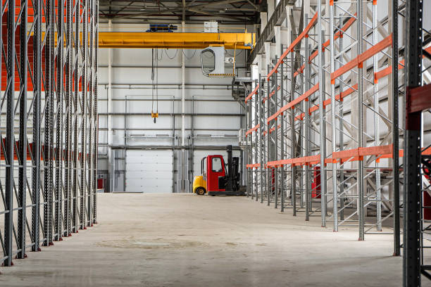 Overhead crane and compact forklift trucks in a empty industrial warehouse building with rows of racks