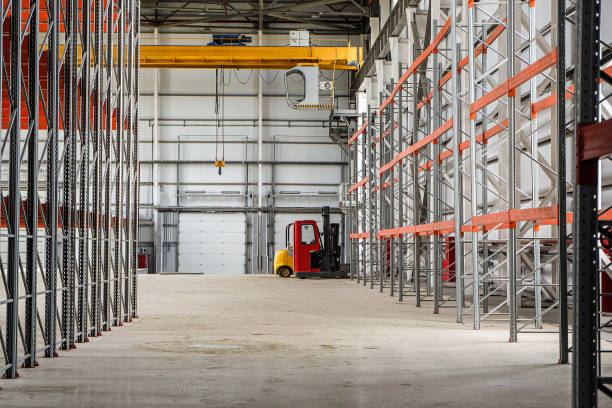 Overhead crane and compact forklift trucks in a empty industrial warehouse building with rows of racks stock photo