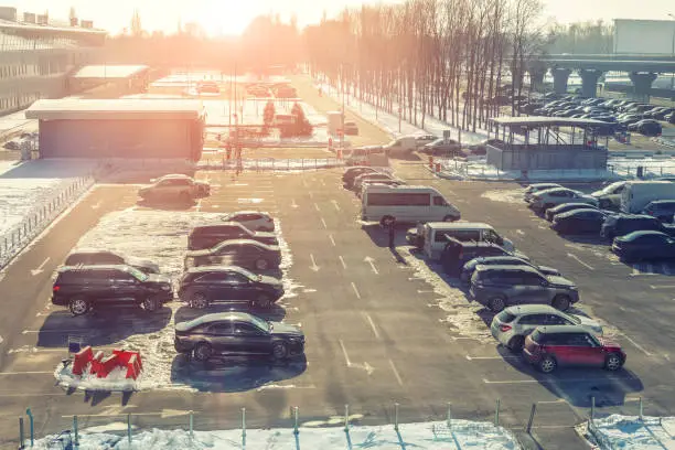 View from above on car parking with many vehicles and free lots at bright early frosty cold winter morning. Parking lot with snowdrifts near airport terminal or shopping business mall at cold weather.