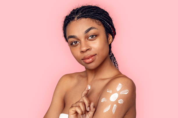 beauty concept. young african woman isolated on pink applying cream on body posing to camera sensual - braids african descent women pensive imagens e fotografias de stock