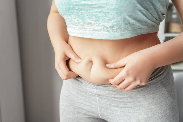 istock Weight Loss. Chubby girl standing in kitchen holding fat fold close-up 1187911043