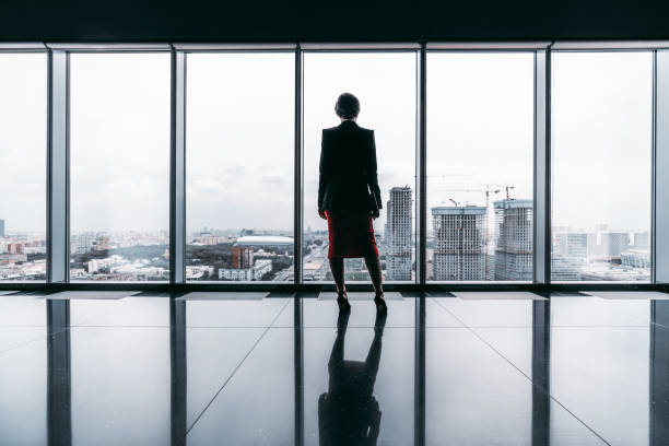 A silhouette of a businesswoman Rearview of a female entrepreneur on the top of a modern business office skyscraper standing near big panoramic windows and pensively looking at cityscape and construction site; floor with reflections observation point stock pictures, royalty-free photos & images