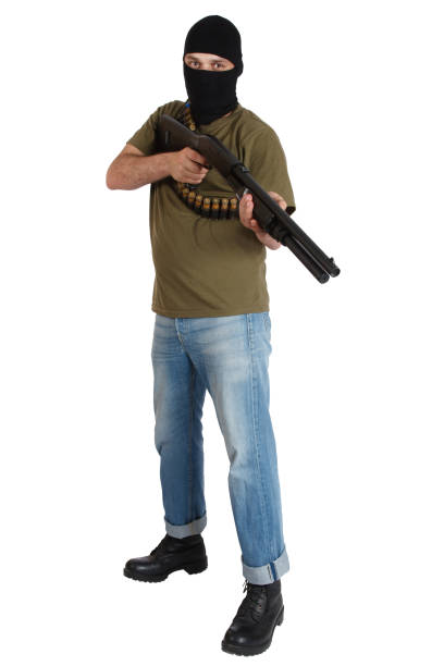 Silhouette of man with assault rifle ready to attack on dark toned foggy background or dangerous bandit in black wearing balaclava and holding gun in hand.