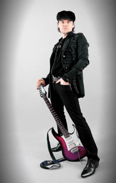 Cool rock guitarist in a hat standing with the electric guitar with retouched/altered guitar headstock on a gray backdrop. Musician posing in a studio. stock photo