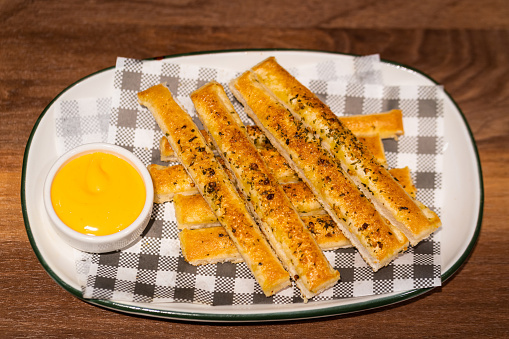 Dish of bread stick with cheesy dipping sauce is served on the wooden table. Close up on delicious food photo.