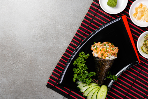 Salmon temaki sushi on black plate on gray background. Japanese cuisine. Top view.